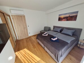 Ett modernt sovrum med en stor säng, en grå soffa, ett litet bord och en tavla på väggen.