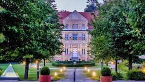 A large, stately building with a symmetrical facade, a central entrance, and a well-maintained garden with a paved pathway leading to the entrance. - Sunday Resort Rugen Junior Suite Manor House (Sagard)
