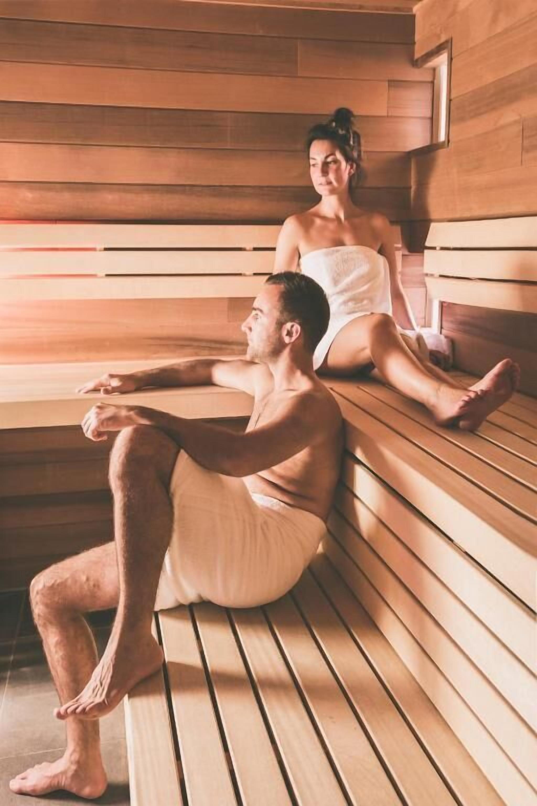 Una sauna con bancos de madera y una persona sentada en uno de ellos.