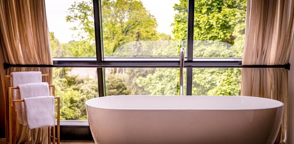A bathroom with a freestanding bathtub, a towel rack with towels, and a large window with curtains.