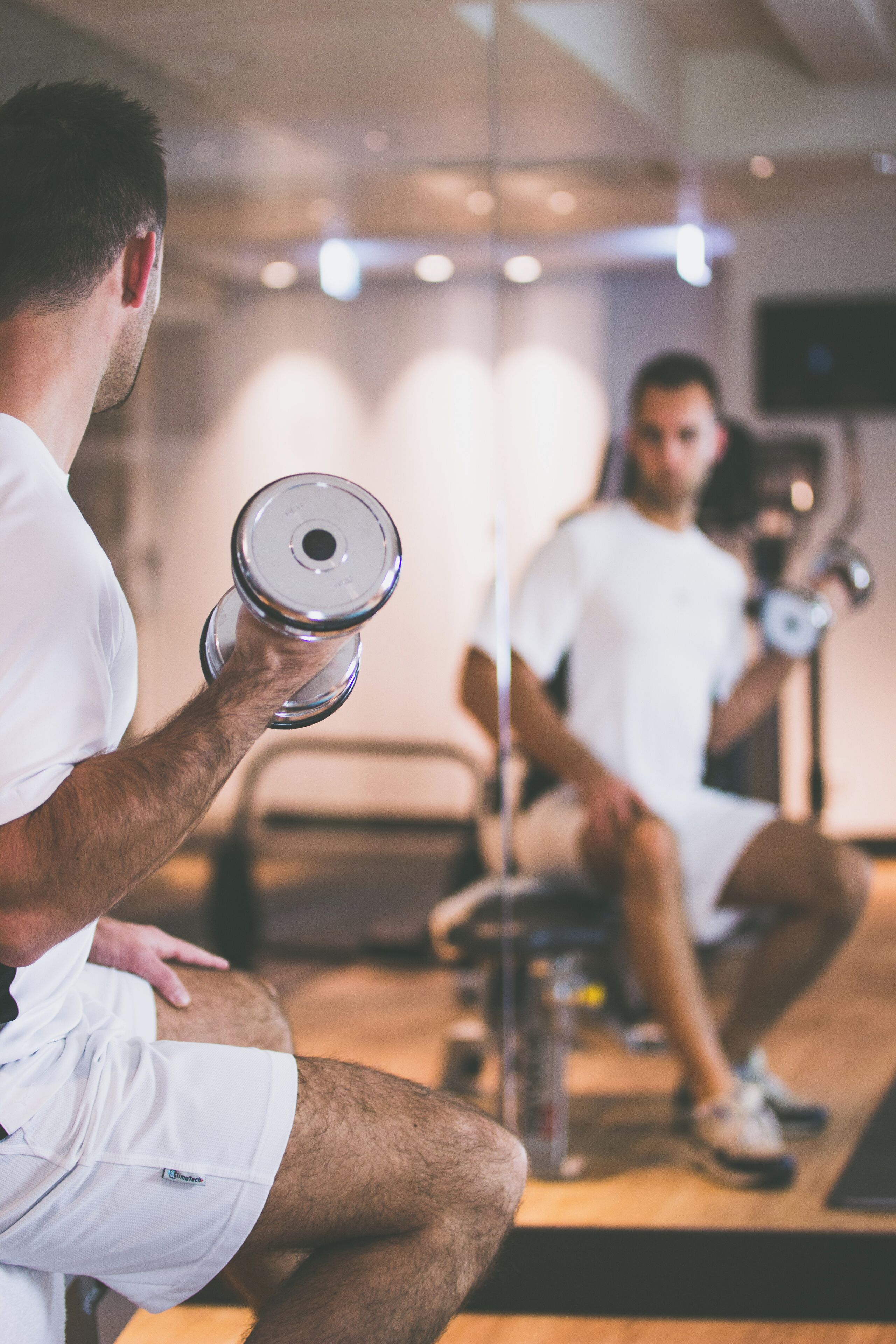 Un gimnasio con espejo, una persona levantando pesas y equipo de ejercicio.