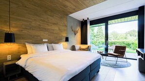 A modern bedroom with a large bed, a seating area, and a view of greenery outside. - Hotel de Sterrenberg (Otterlo)