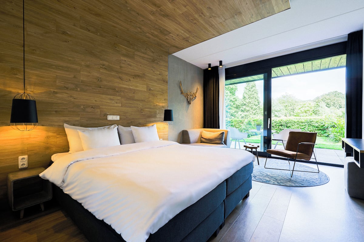 Ein modernes Schlafzimmer mit einem großen Bett, einer Sitzecke und Blick ins Grüne.