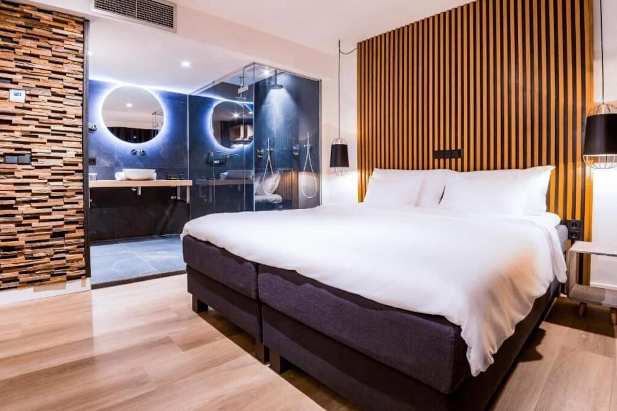 Ein modernes Schlafzimmer mit einem großen Bett, einer Holzvertäfelung, einem verglasten Badezimmer und einem runden Spiegel.