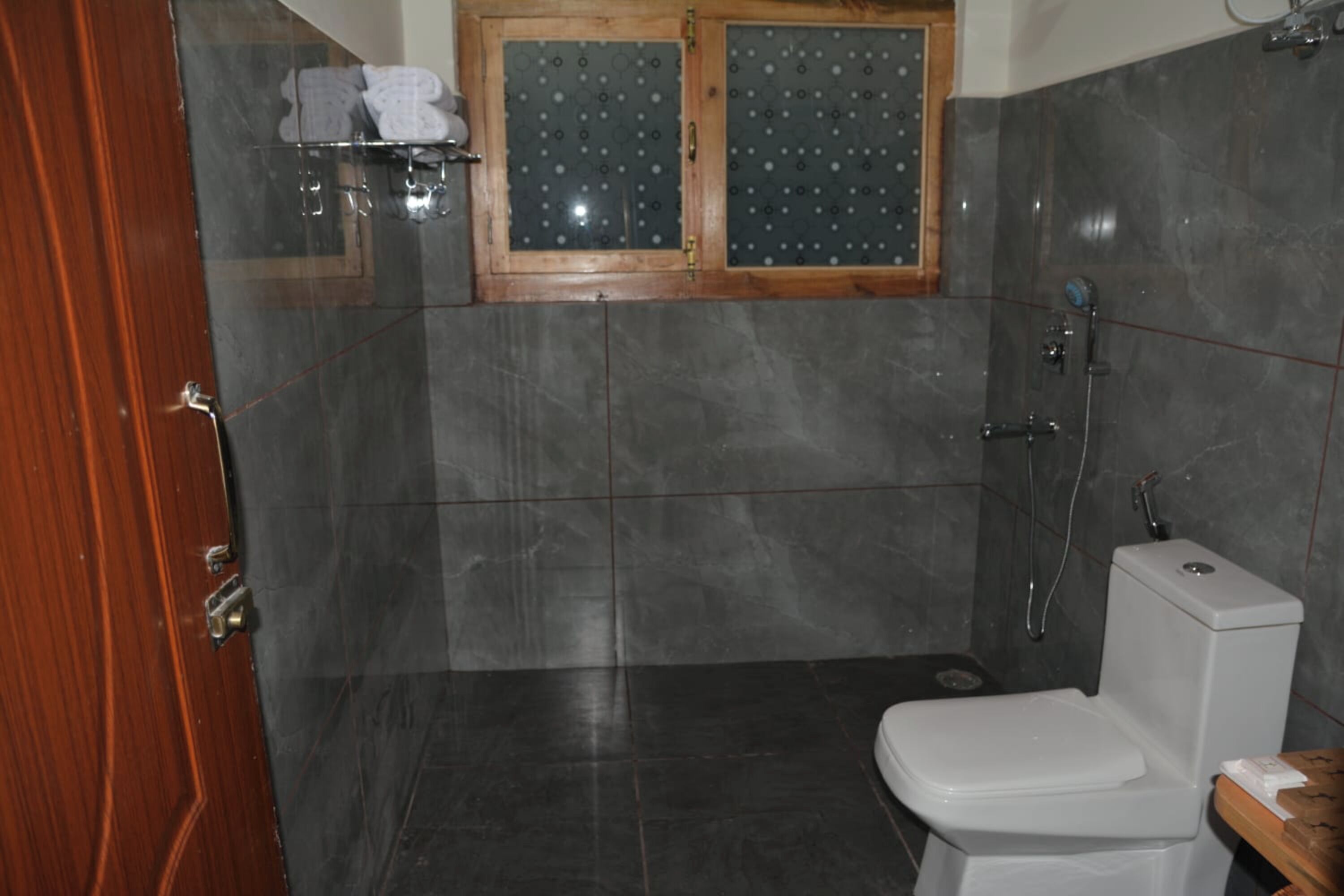 A bathroom with a toilet, a shower, and a window with frosted glass.