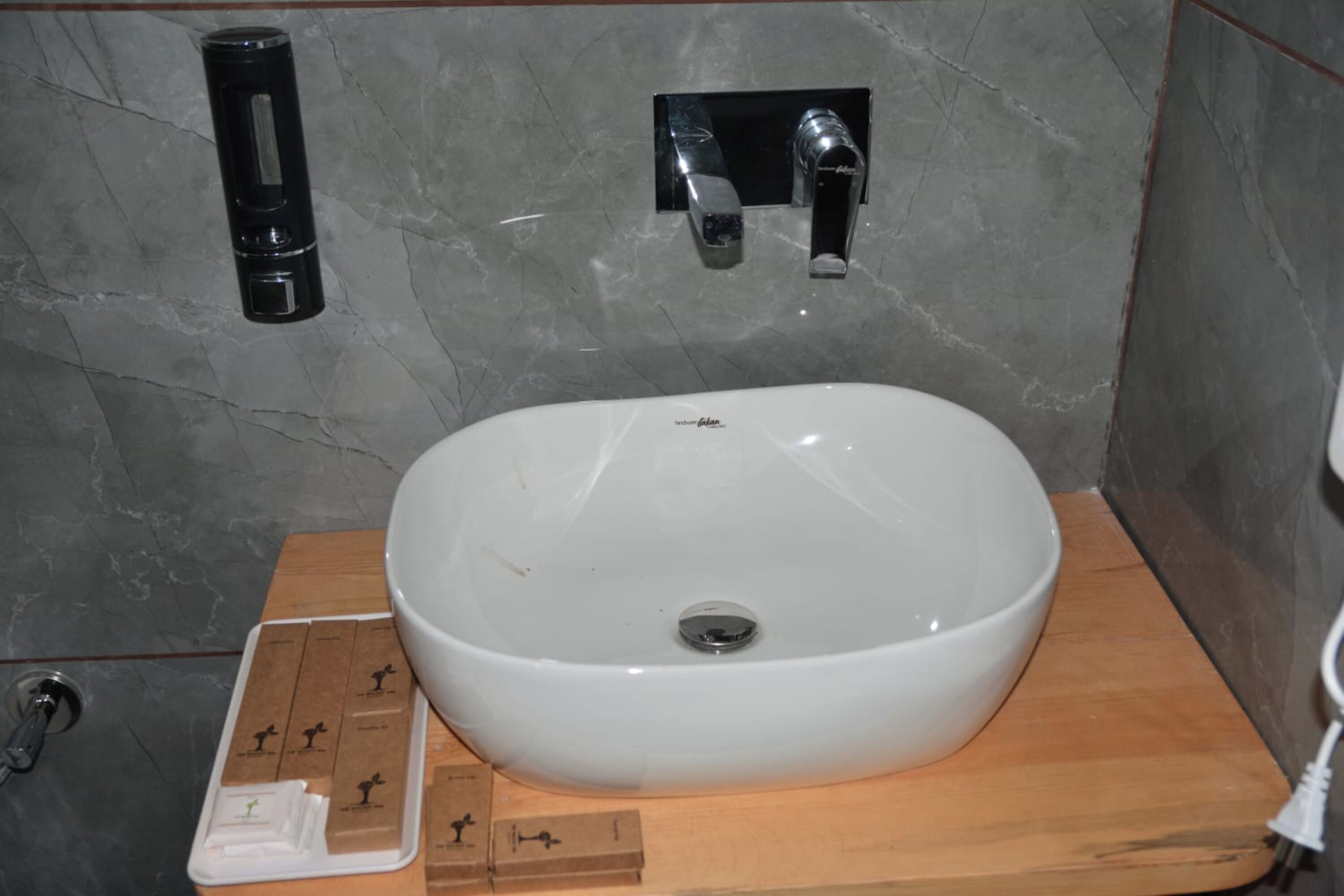 A bathroom with a white sink, a black soap dispenser, and a wooden vanity.