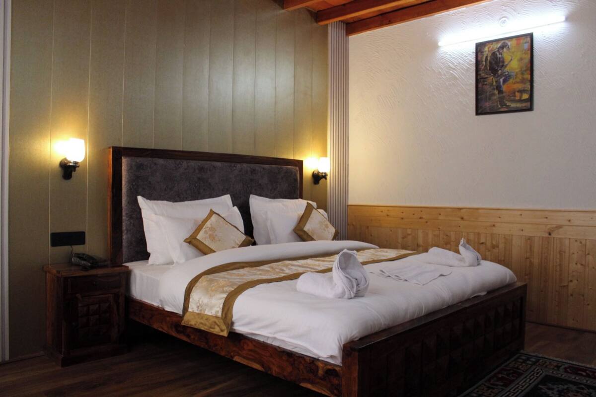 A neatly made bed with white linens and a brown headboard, two bedside tables with lamps, and a wooden headboard panel.