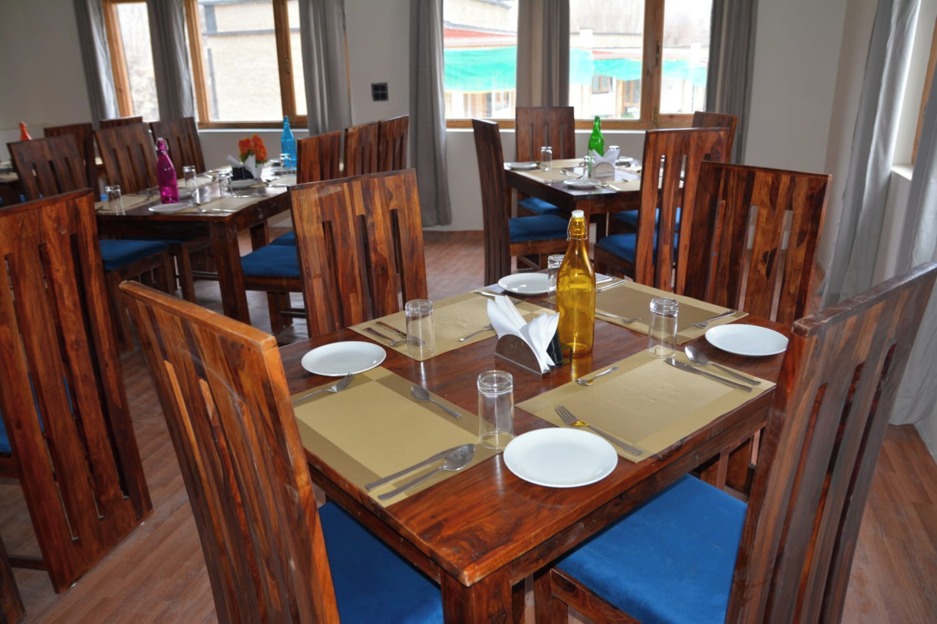 Un comedor con mesas y sillas de madera, dispuesto para una comida.