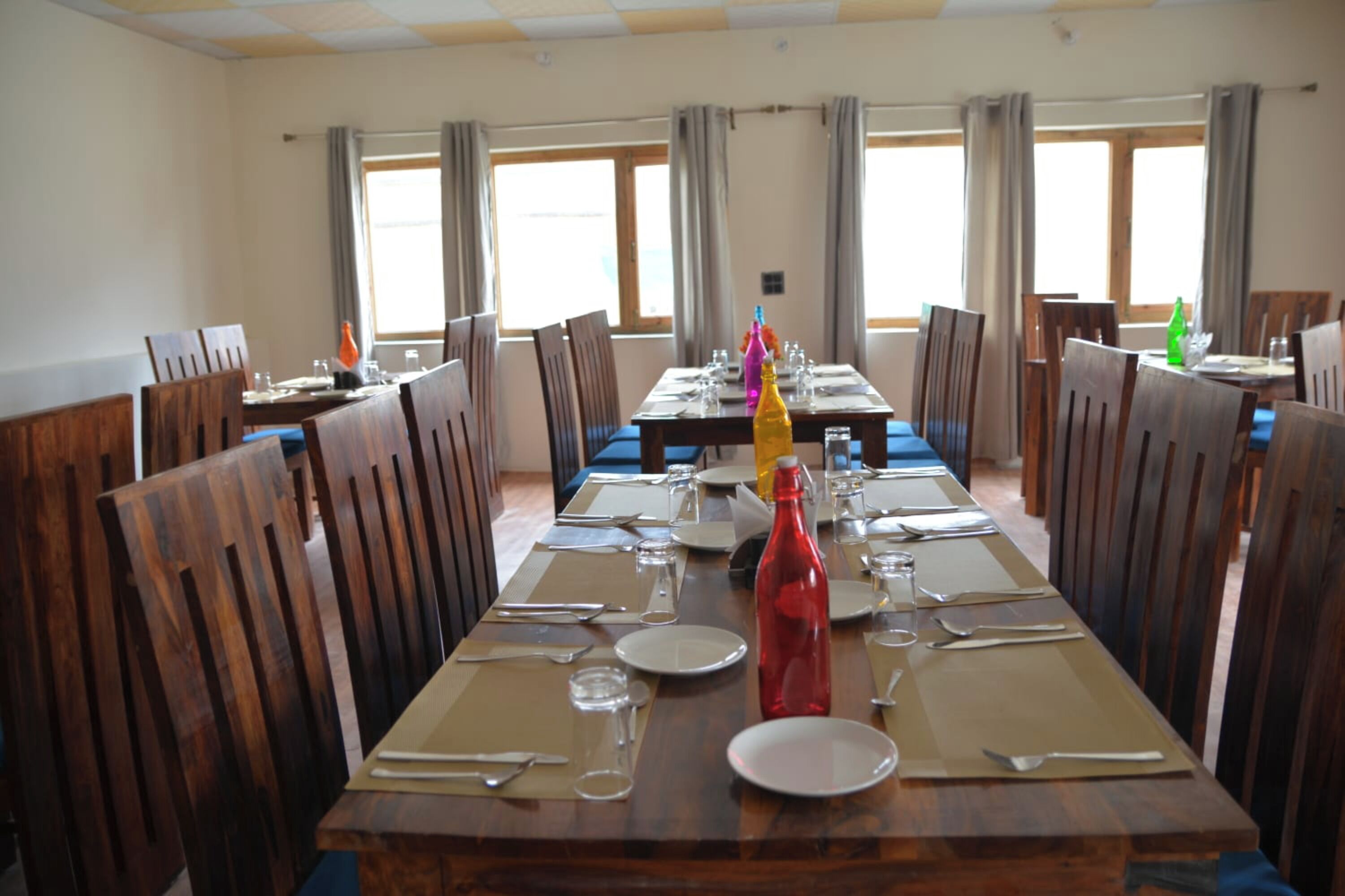 Comedor con mesas y sillas de madera, dispuesto para una comida.