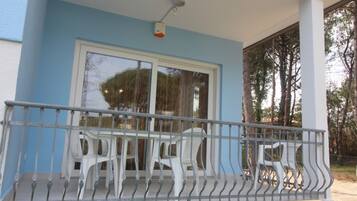 A balcony with a metal railing, two white plastic chairs, and a large window with a view of trees.