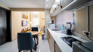 A modern kitchen with a dining area, a TV, and a window with blinds. - The Linkview Shortlet Apartment (Lekki)