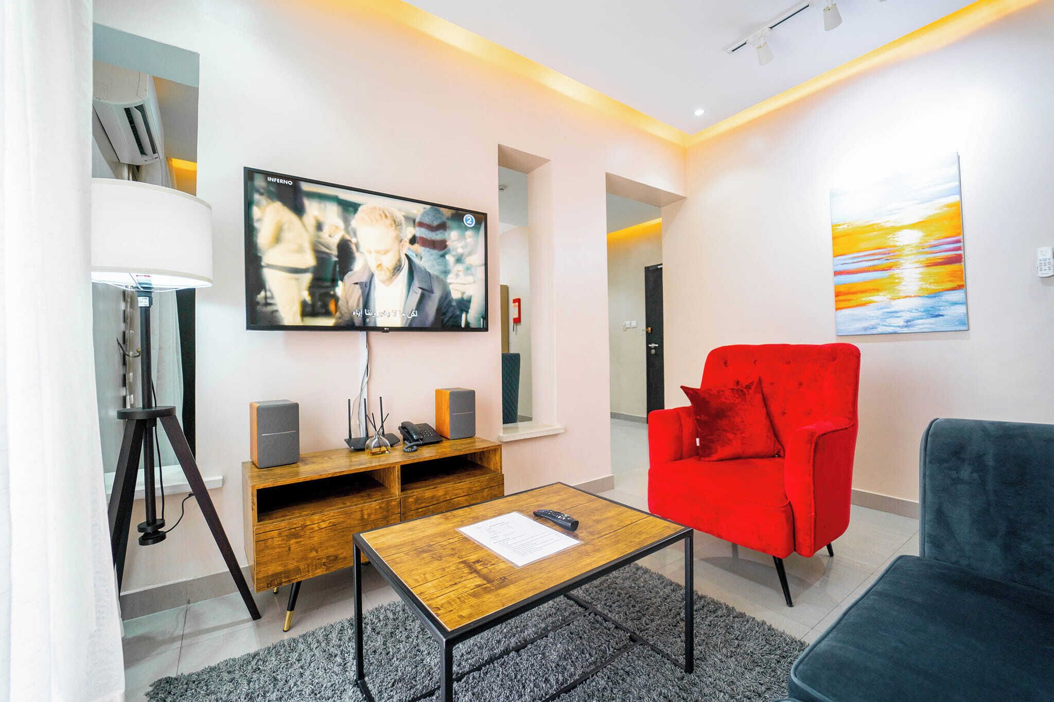Una sala de estar moderna con un televisor de pantalla plana, un sillón rojo, un sofá azul y una mesa de centro de madera.