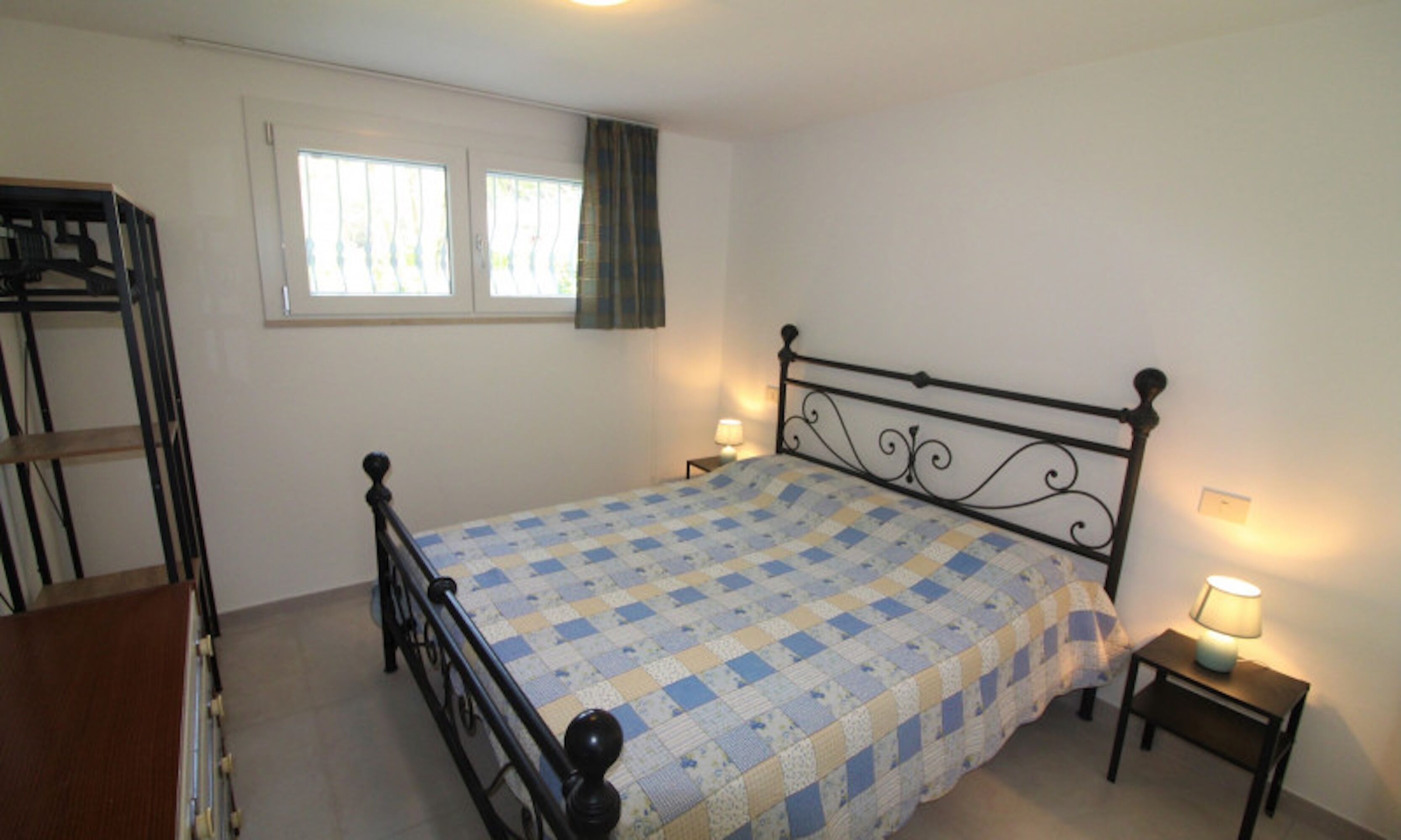Una camera da letto con un letto, due comodini con lampade, una finestra con tende e una struttura a letti a castello.