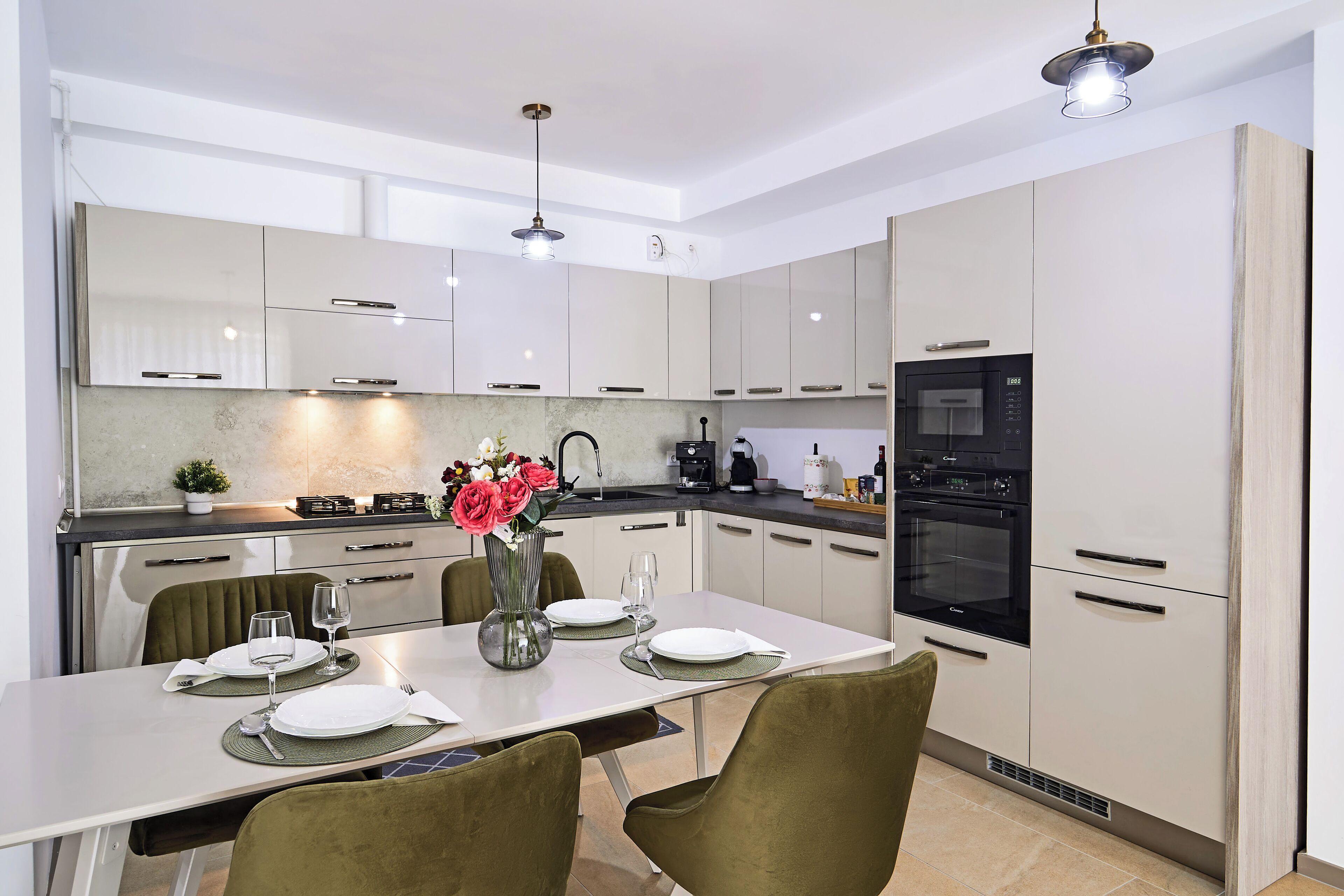 A modern kitchen with white cabinets, a dining table set for four, and a vase with flowers.