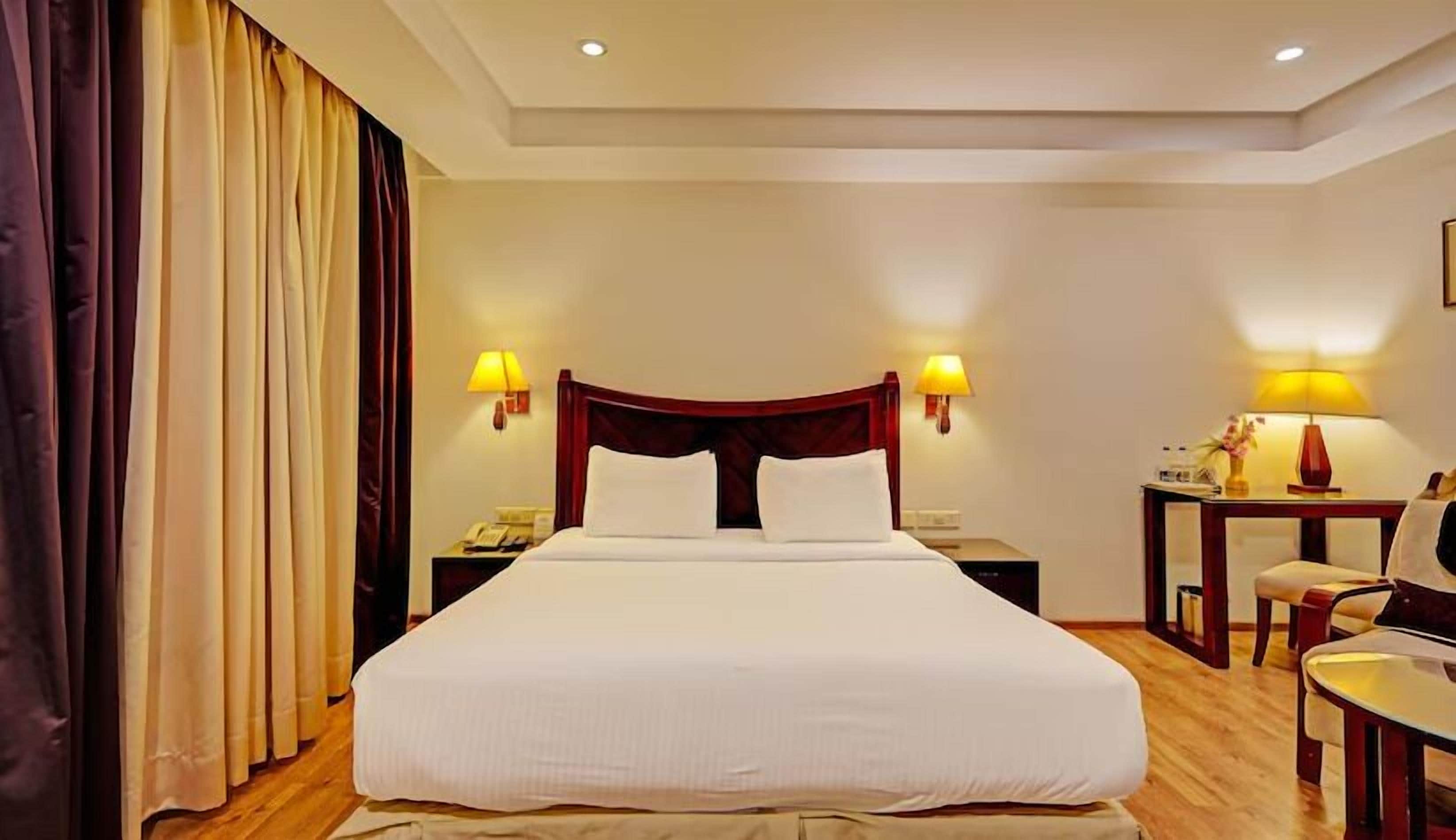 Habitación de hotel con una cama grande, dos mesitas de noche con lámparas, un escritorio con silla y una ventana con cortinas.