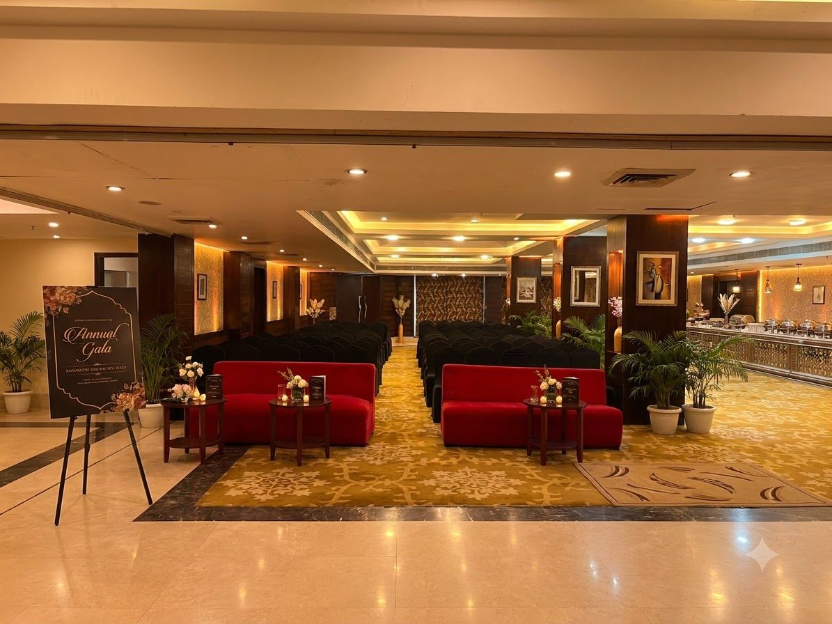 A hotel lobby with a reception desk, red sofas, a carpeted floor, and a decorative wall.