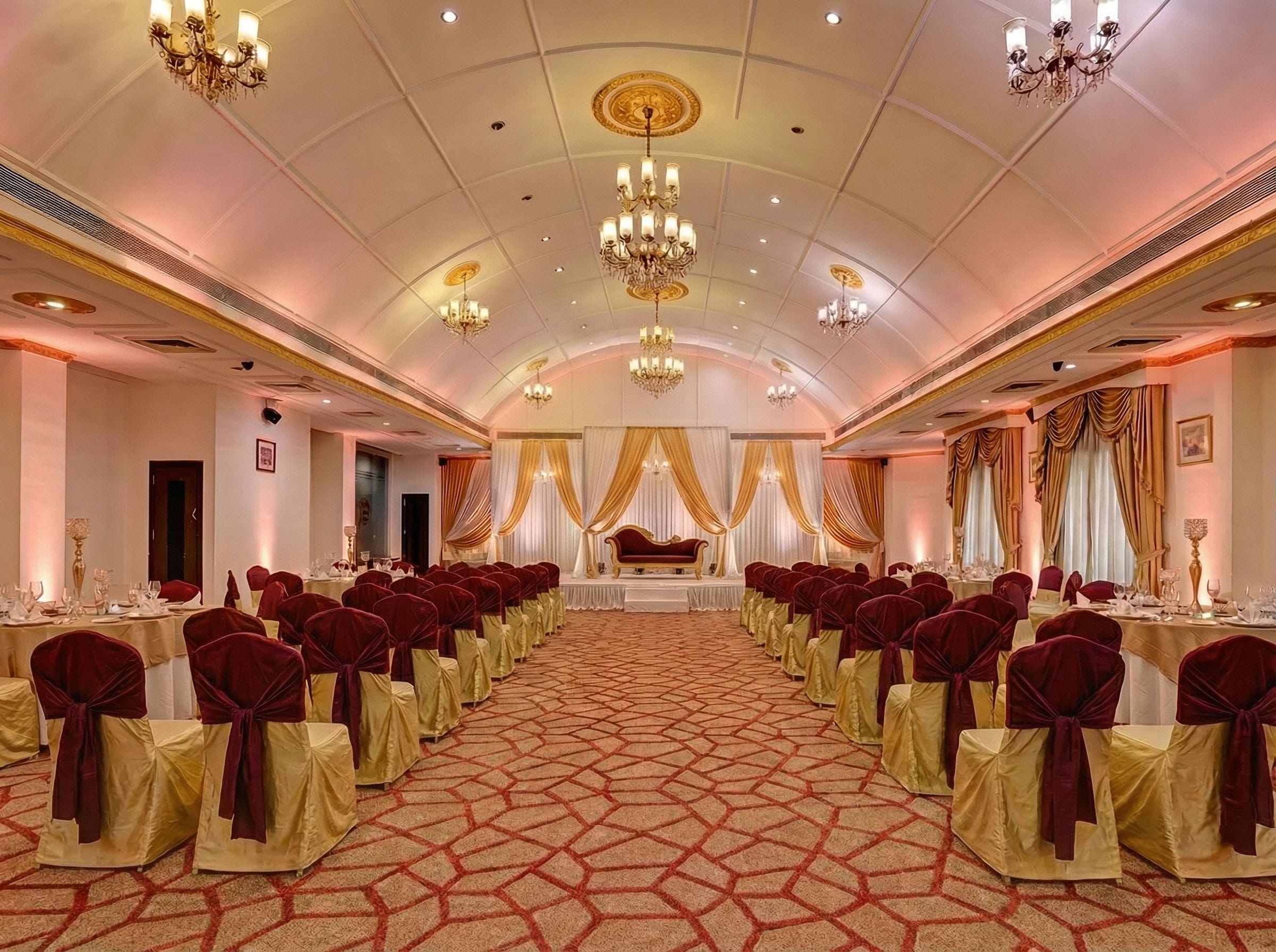 A banquet hall with rows of tables, chairs, and a stage with draped curtains.