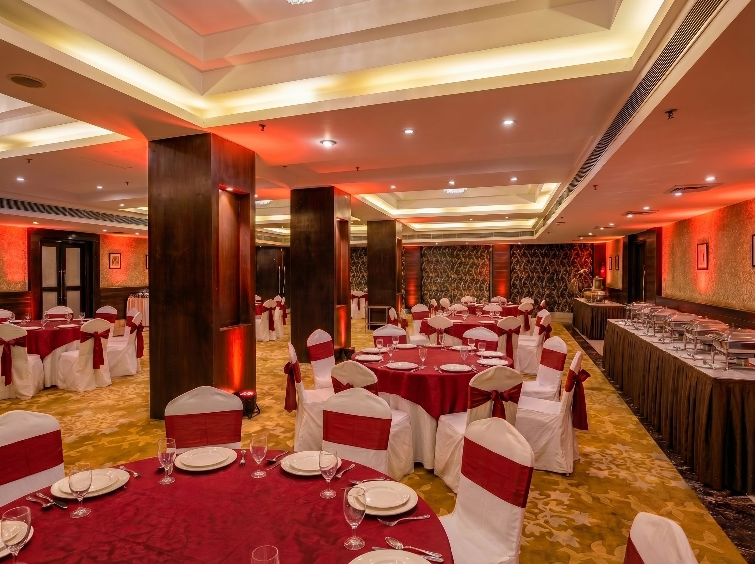 A banquet hall with round tables, white chairs with red sashes, and a carpeted floor.