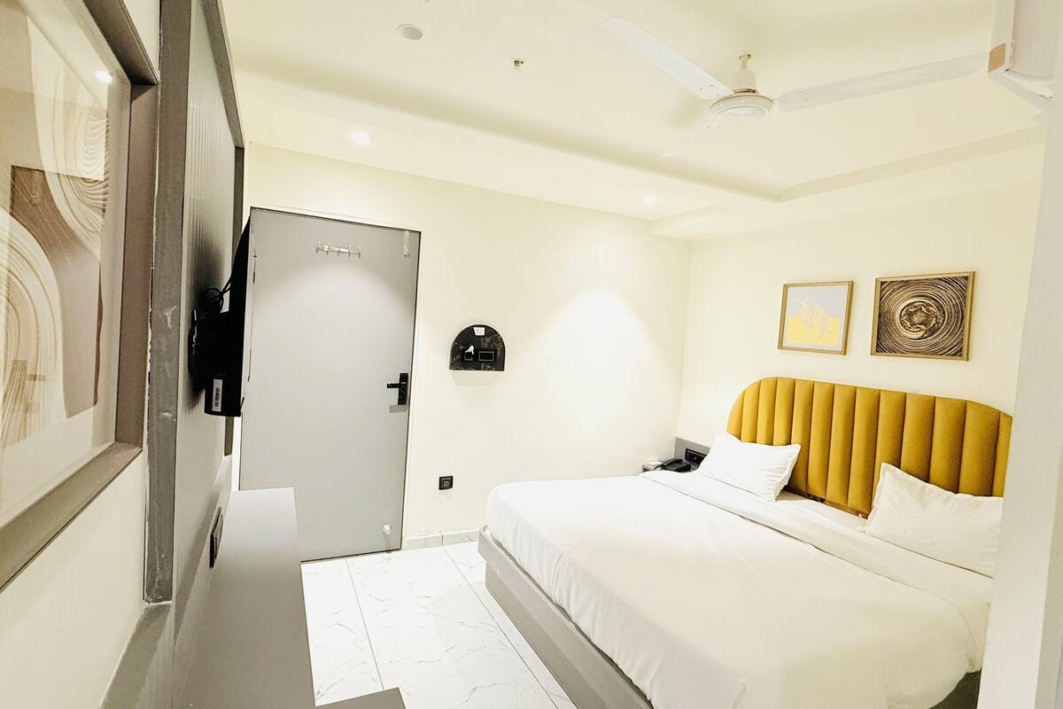 A hotel room with a bed, a ceiling fan, a door, and a wall-mounted TV.