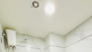 A modern bathroom with a white toilet, a shower unit, and a marble-patterned wall. - Hotel Maple Town (Ahmedabad)