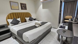 A hotel room with a bed, bedside table, chair, and a small table with a lamp. - Hotel Maple Town (Ahmedabad)