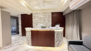 A reception area with a marble counter, a wooden panel, and a grey sofa. - Hotel Maple Town (Ahmedabad)