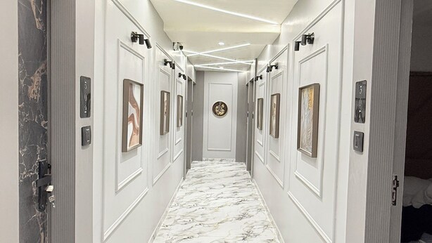 A hallway with a marble floor, white walls, and framed artwork on the walls. - Hotel Maple Town (Ahmedabad)