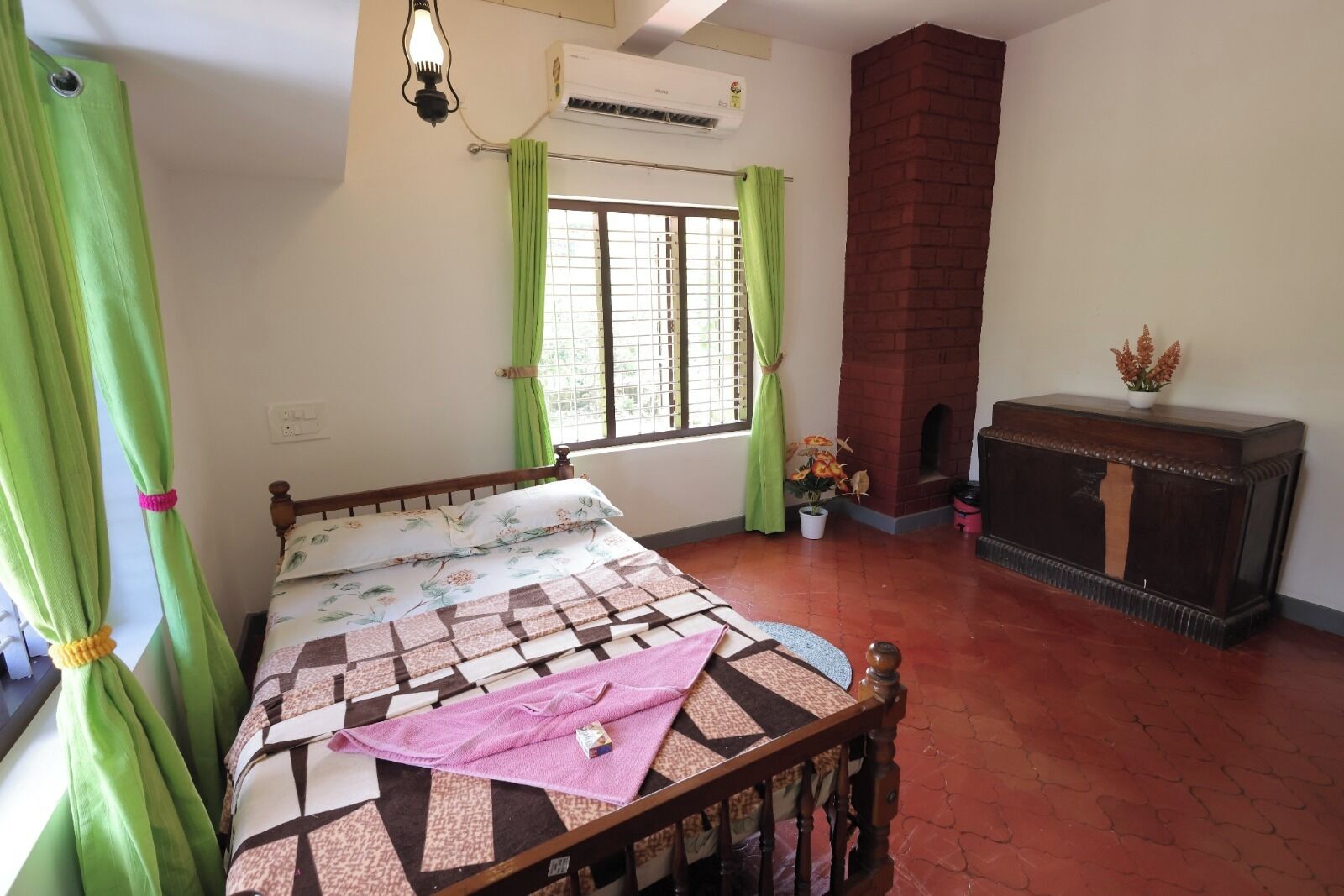A bedroom with a bed, a fireplace, a window with curtains, and a potted plant.