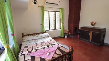 A bedroom with a bed, a fireplace, a window with curtains, and a potted plant.