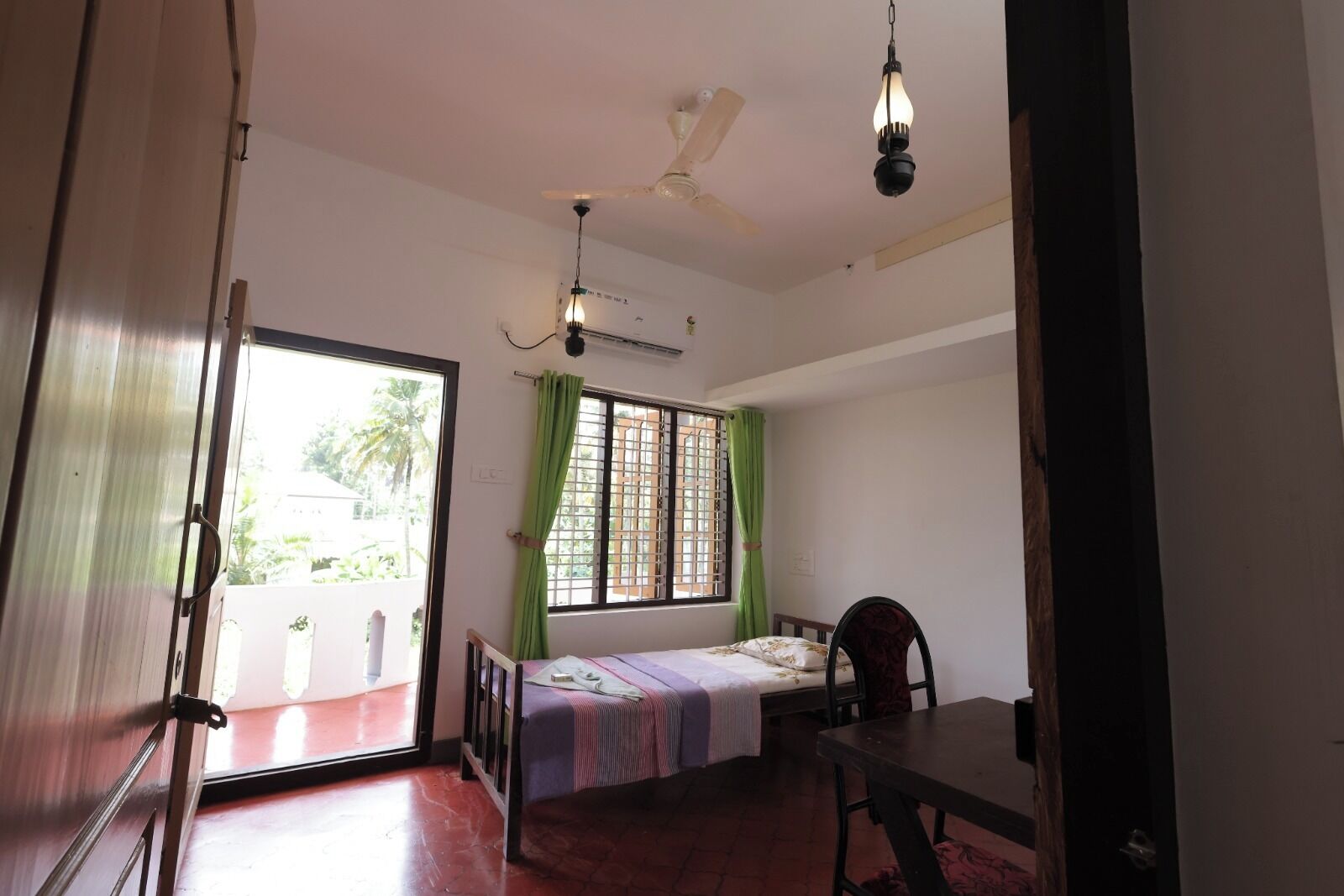 A room with a bed, a table, a ceiling fan, and a window with curtains.
