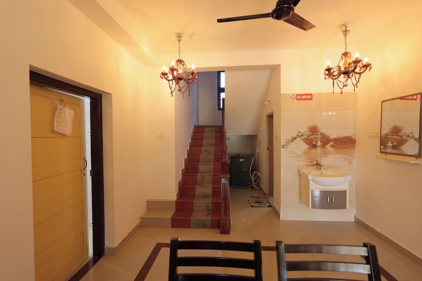 A hallway with a staircase, a dining area with chairs, a chandelier, a ceiling fan, and a 'No Smoking' sign.