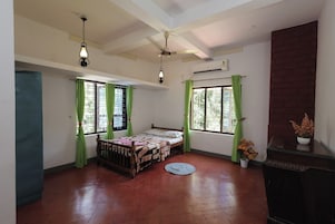 Un dormitorio con cama, dos ventanas con cortinas verdes, ventilador de techo y pared de ladrillo.