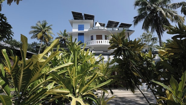 Um edifício branco com painéis solares no telhado, cercado por plantas tropicais.