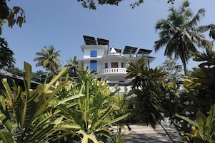 Un edificio blanco con paneles solares en el techo, rodeado de plantas tropicales.