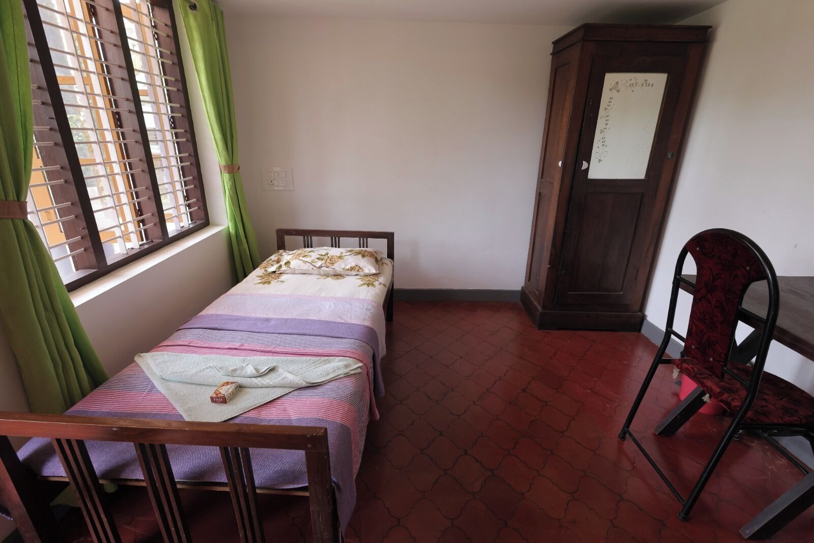 Una habitación pequeña y ordenada con una cama individual, una silla de madera y un armario.