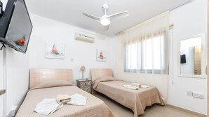 Une chambre d’hôtel avec deux lits, un ventilateur de plafond, des œuvres d’art accrochées aux murs et une fenêtre avec des rideaux.
