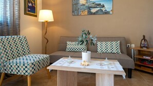 Una sala de estar acogedora con un sillón estampado, un sofá con cojines a juego, una mesa con adornos y un cuadro de una escena costera en la pared.