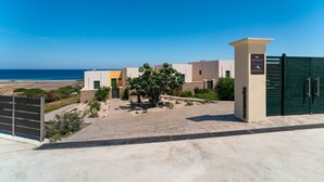 Complejo moderno de edificios con entrada porticada, vista despejada a la playa y un cartel que indica 'Mare Blue 1'.