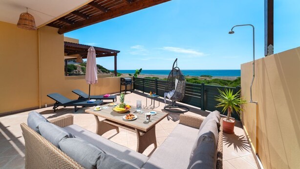 Un patio al aire libre con muebles de mimbre, una mesa con comida, una silla colgante y vistas al mar.