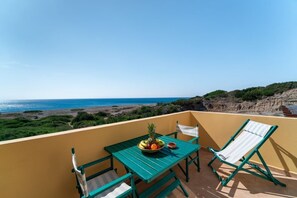Un balcón con una mesa dispuesta para dos, una silla y vista al mar.