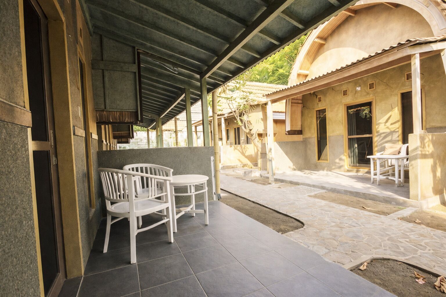 A covered outdoor area with a seating arrangement and a stone pathway leading to a building with a tiled roof.