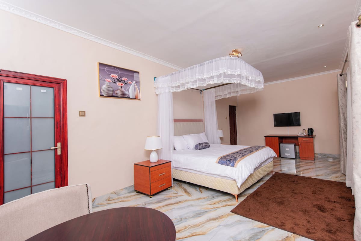 A hotel room with a bed, a desk, a TV, and a red door.