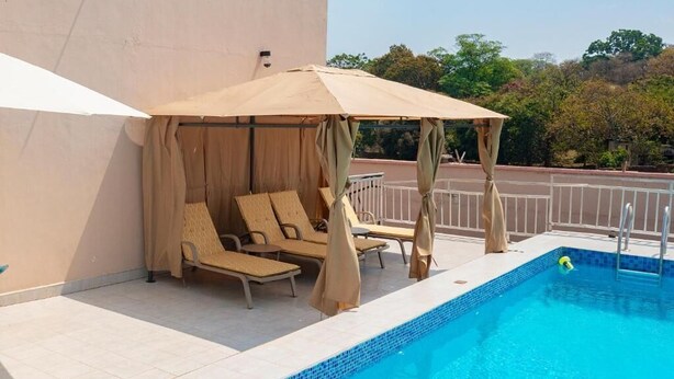 A poolside area with a covered seating area and a pool. - Lavish Suites (Blantyre)