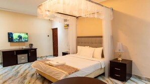 A four-poster canopy bed with a television on a stand, a bedside table, and a lamp. - Lavish Suites (Blantyre)