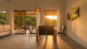 Una sala de estar moderna con comedor, puertas correderas de vidrio grandes y vistas a un paisaje boscoso.