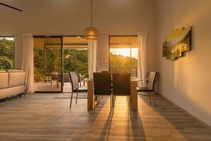 Een moderne woonkamer met een eethoek, grote schuiframen en uitzicht op een bebost landschap.