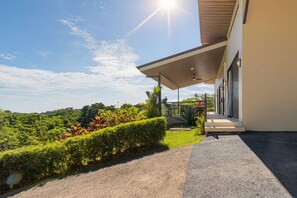 Un bâtiment moderne doté d’un espace extérieur abrité, entouré d’une végétation luxuriante et surplombé d’un ciel dégagé.