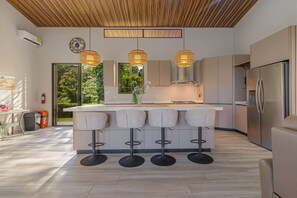 Une cuisine moderne dotée d’un îlot central, de tabourets de bar, de luminaires suspendus et d’un réfrigérateur en acier inoxydable.