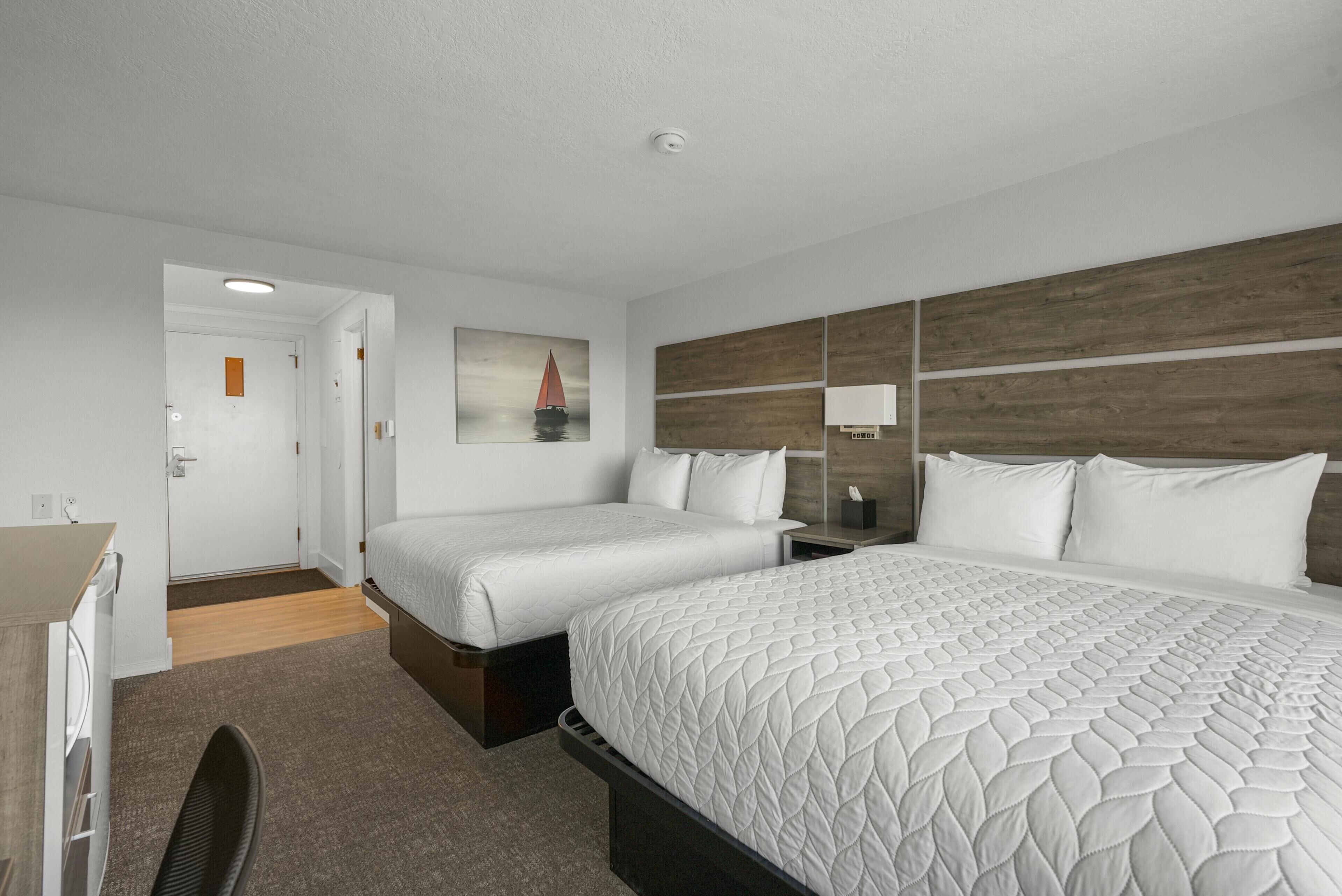 Habitación de hotel con dos camas, un escritorio, una silla, un cuadro y un cabecero de madera.