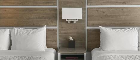 Habitación de hotel con dos camas, una mesita de noche con lámpara y cabecero de madera.